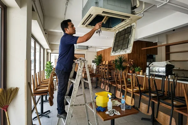 Technician cleaning a 4-way ceiling cassette in a café after closing