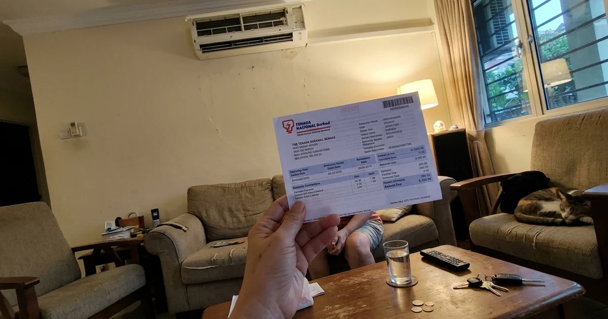 Homeowner holding a TNB electricity bill in a living room with the aircon running