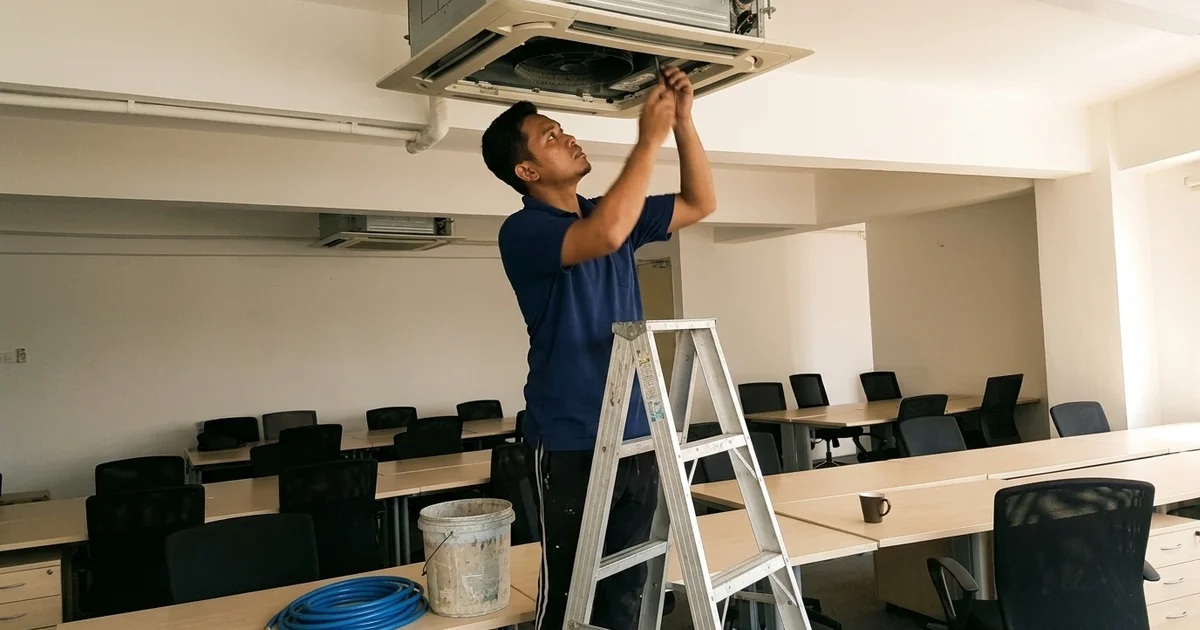 Technician servicing a ceiling cassette in a small KL office after hours