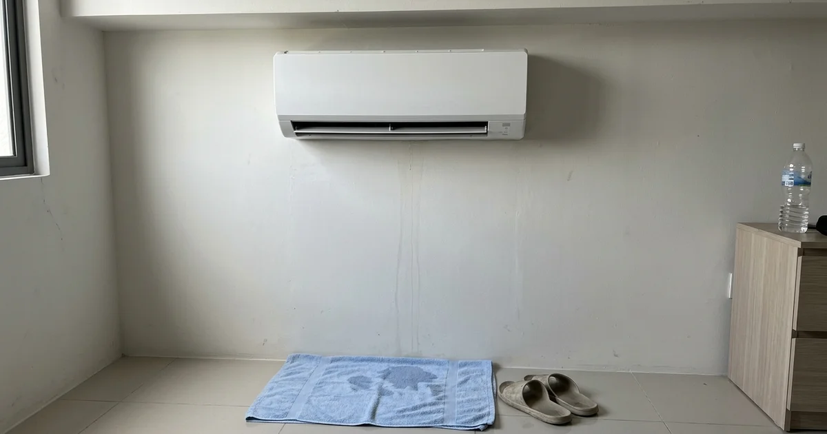 Water stain on the wall below a dripping aircon with a towel on the floor